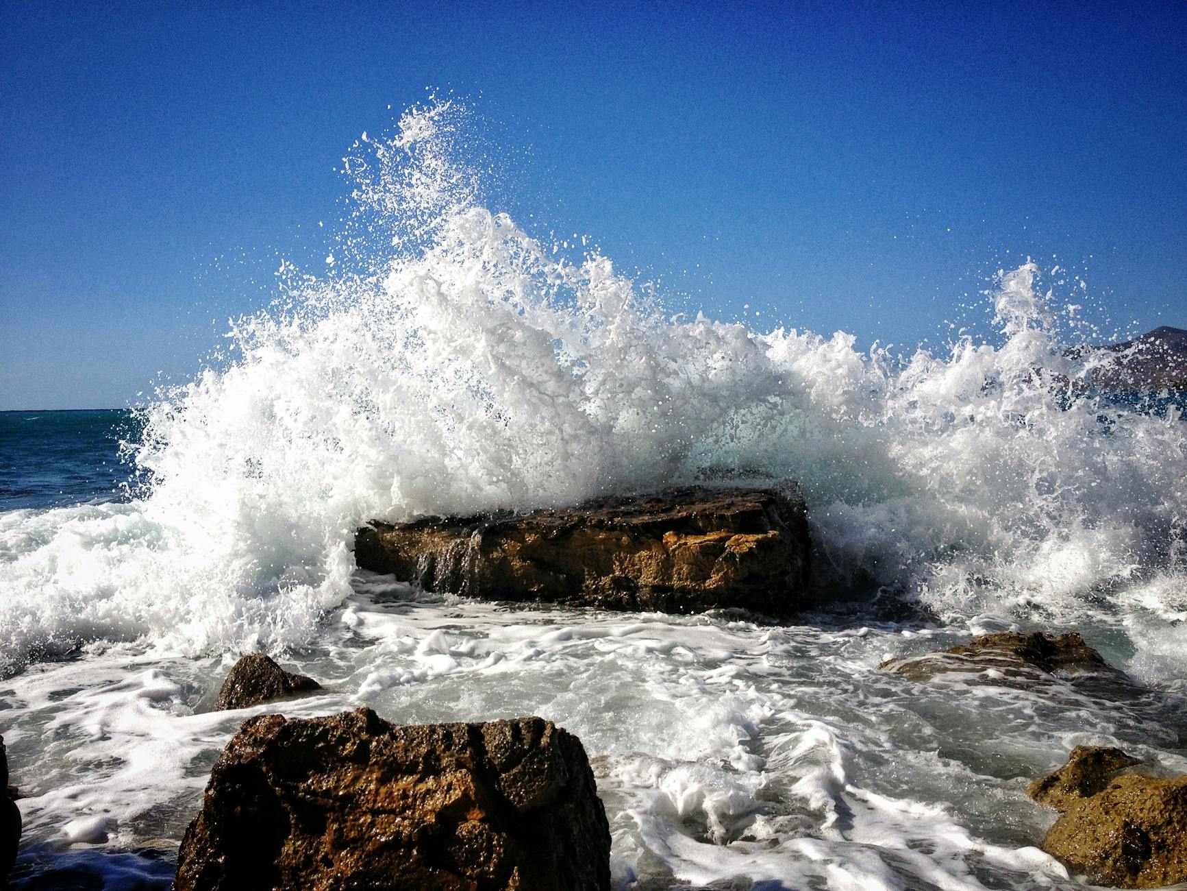 rocky seashore with ocean wave under blue sky