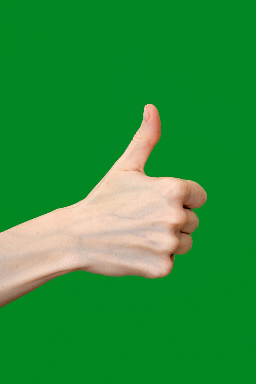 close up of a hand showing thumbs up on green background