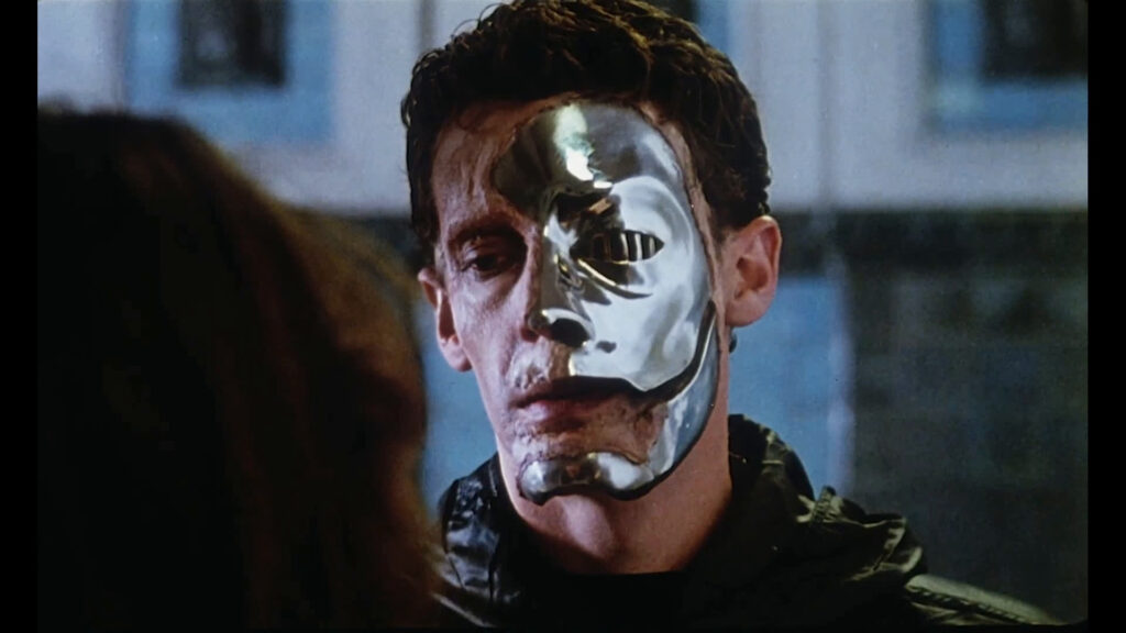 A still from Demons (1985) depicting a man wearing a metal half mask.